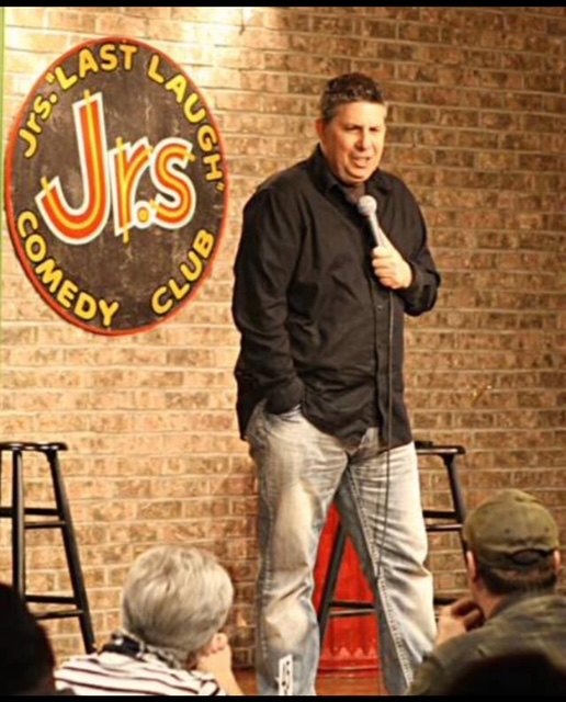 A comedian performing with a microphone on a comedy-club stage