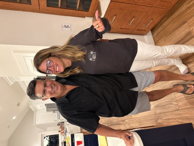 Greg and a guest smiling together in a kitchen